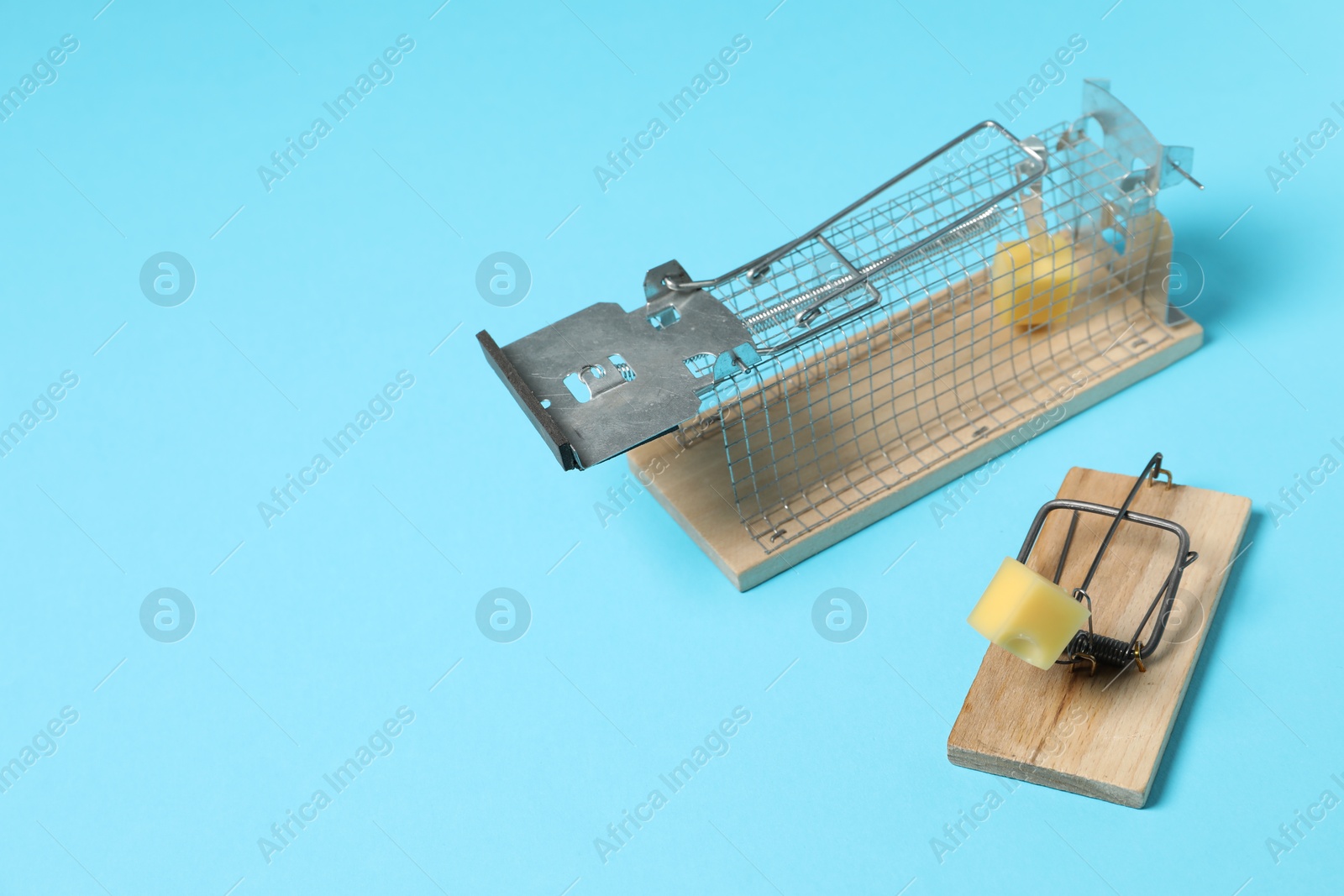 Photo of Two different mouse traps with bait on light blue background, space for text