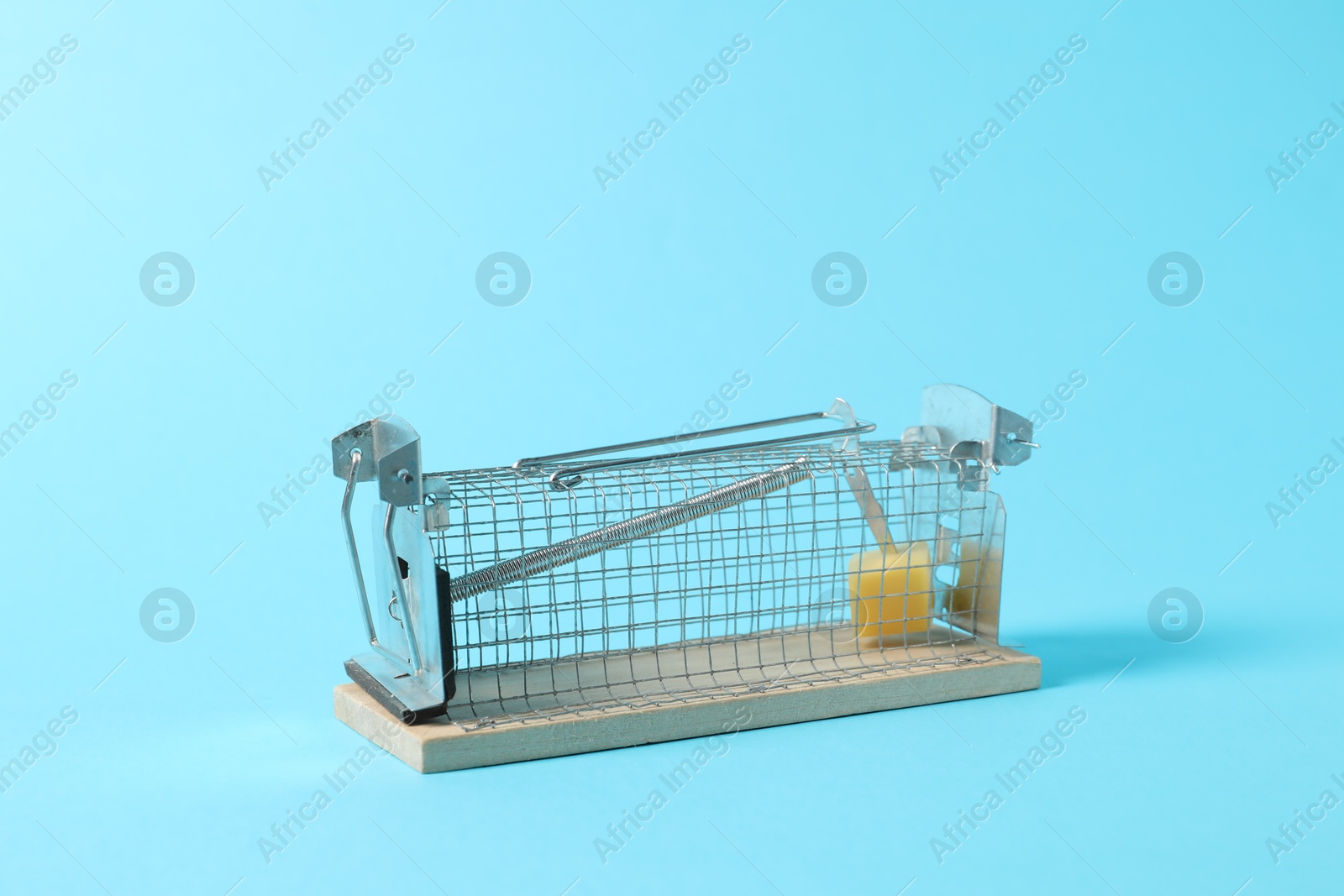 Photo of Metal mouse trap with piece of cheese on light blue background