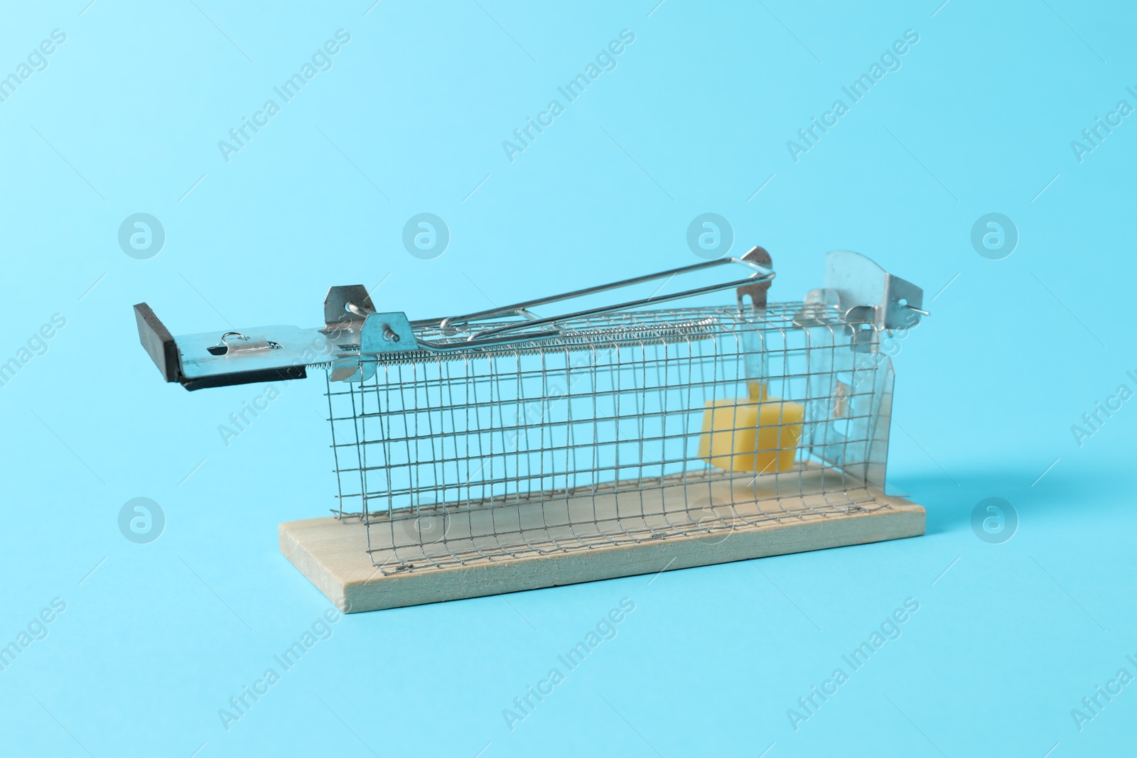 Photo of Metal mouse trap with piece of cheese on light blue background