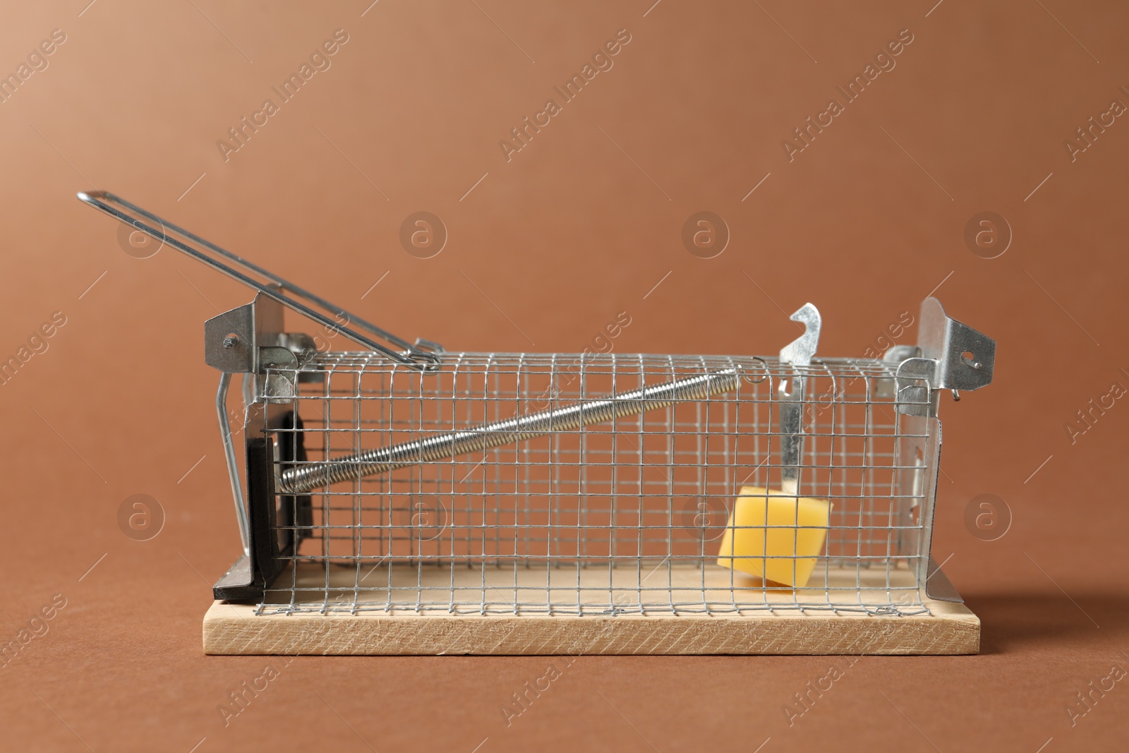 Photo of Metal mouse trap with piece of cheese on brown background