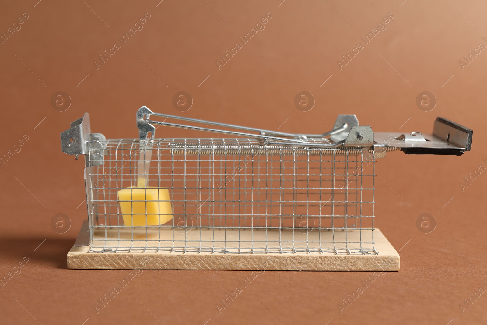 Photo of Metal mouse trap with piece of cheese on brown background