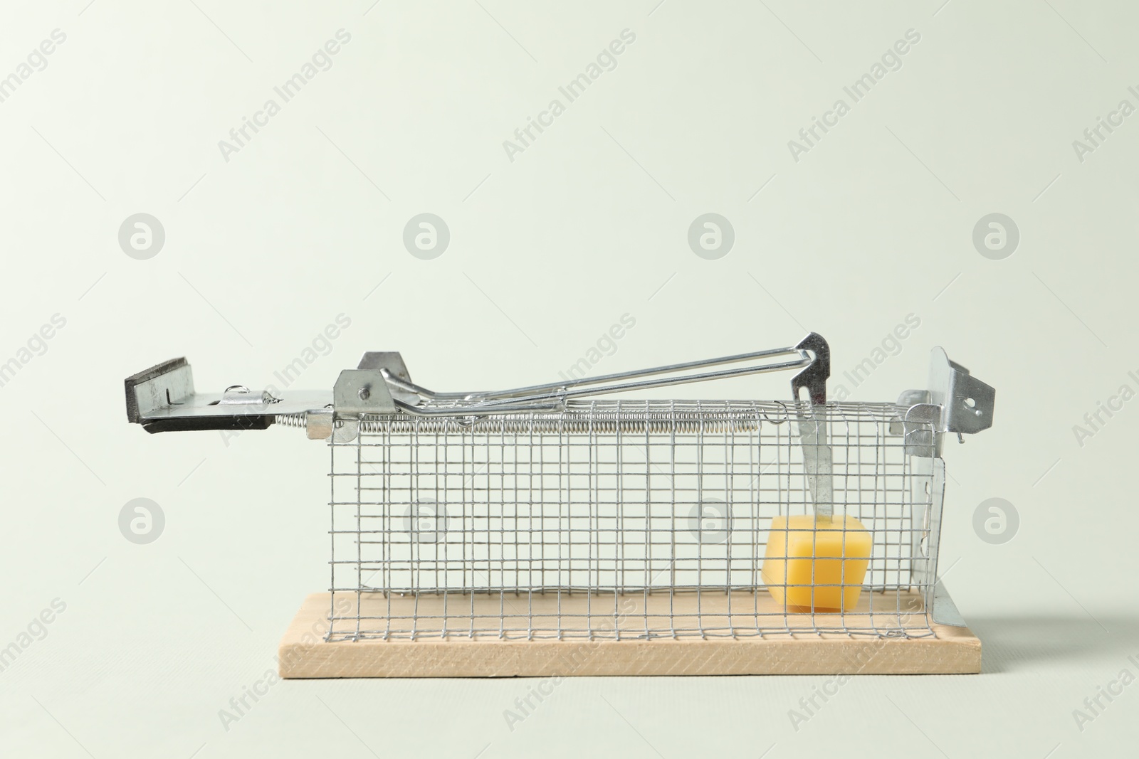 Photo of Metal mouse trap with piece of cheese on light background