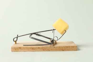 Photo of Spring-loaded bar mousetrap with piece of cheese on light background