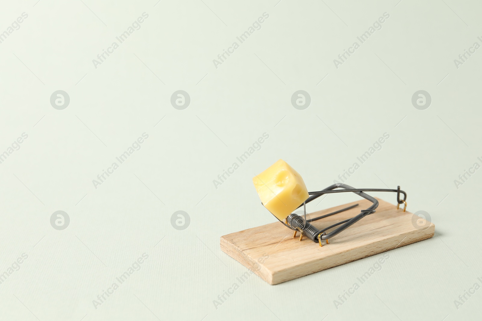 Photo of Spring-loaded bar mousetrap with piece of cheese on light background, space for text