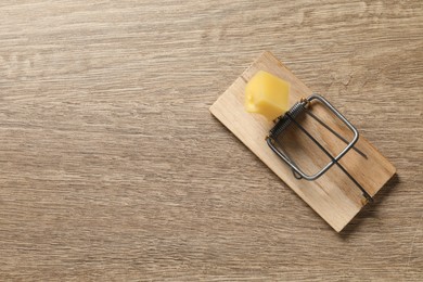 Photo of Spring-loaded bar mousetrap with piece of cheese on floor, top view. Space for text