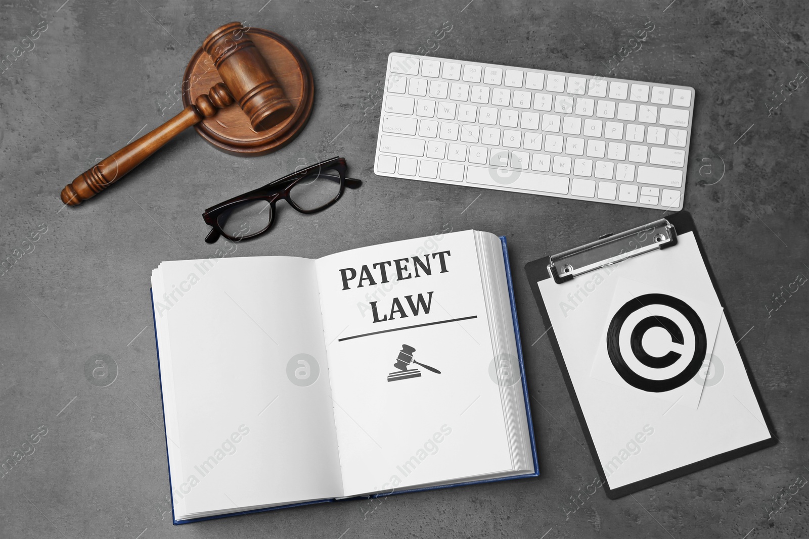 Image of License. Patent law book, paper with copyright symbol, computer keyboard and judge's gavel on grey table, flat lay