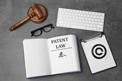 Image of License. Patent law book, paper with copyright symbol, computer keyboard and judge's gavel on grey table, flat lay