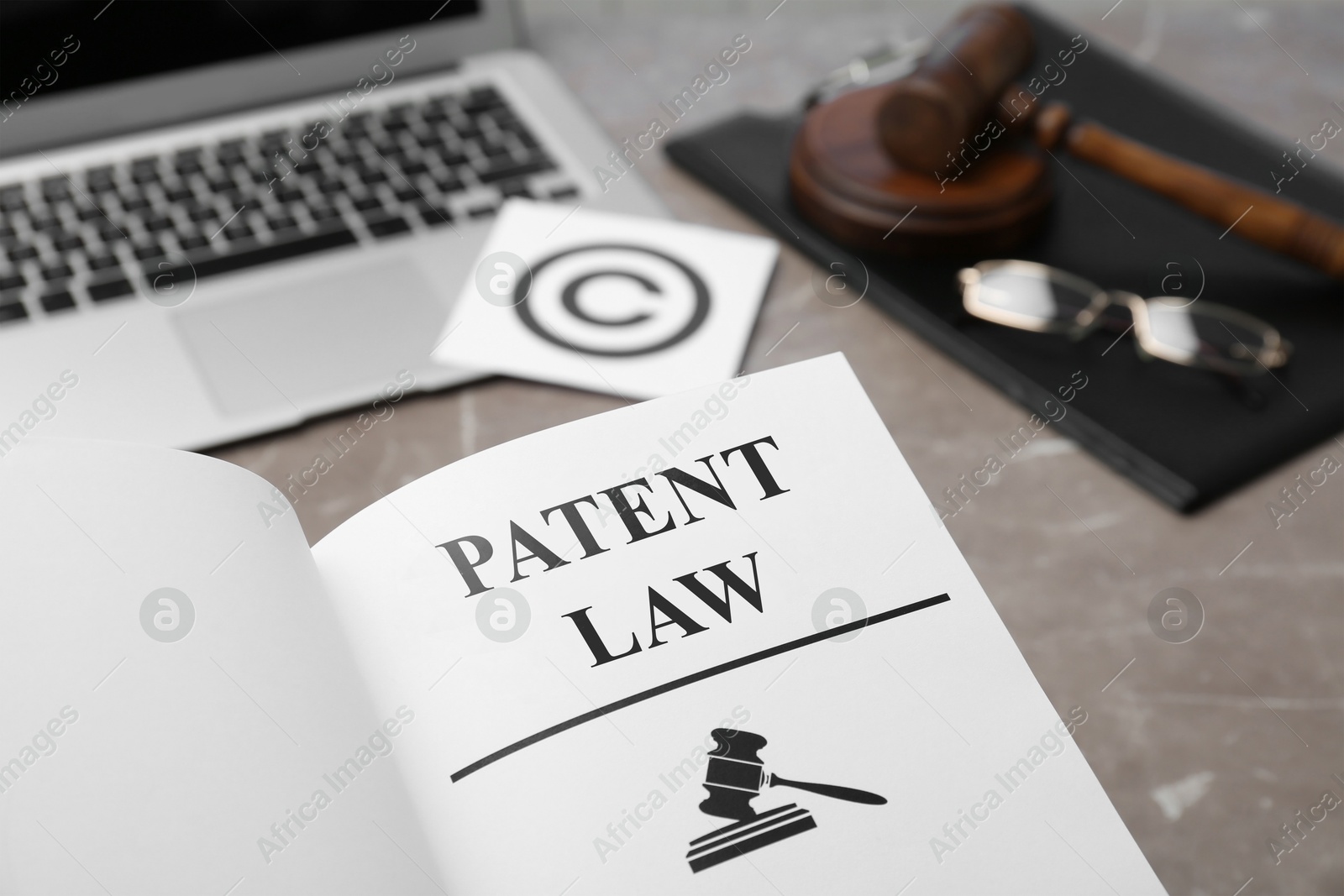 Image of License. Patent law book, laptop, paper with copyright symbol and judge's gavel on grey table, closeup