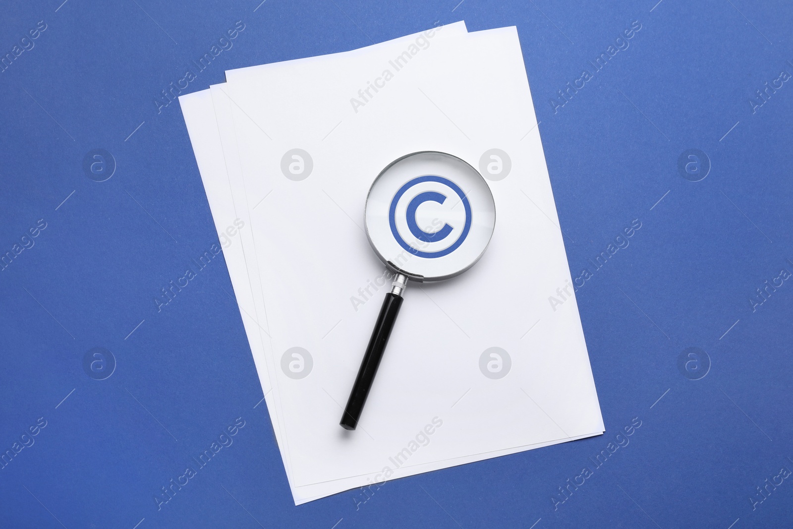 Image of License. Paper with copyright symbol and magnifying glass on blue background, top view