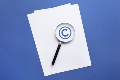 Image of License. Paper with copyright symbol and magnifying glass on blue background, top view