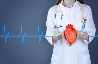 Image of Cardiology. Doctor holding anatomical model of heart on color background, closeup. Blue heartbeat line