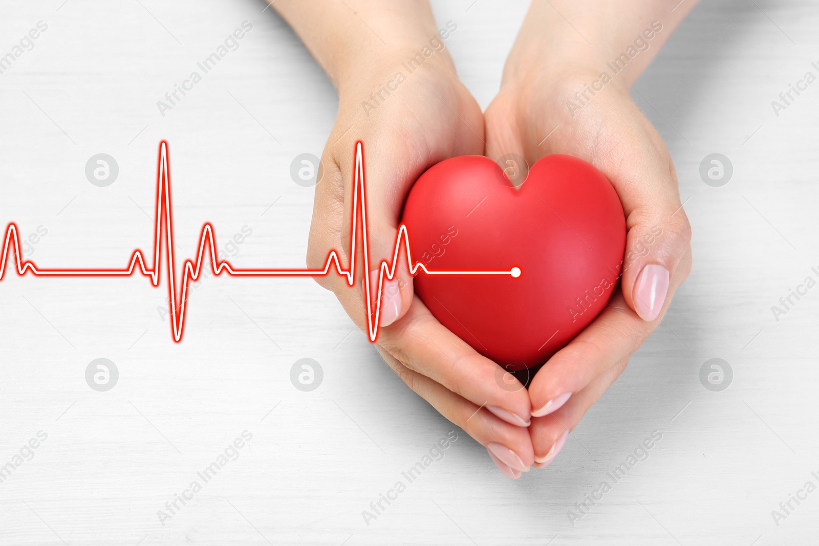 Image of Cardiology. Woman holding red decorative heart on white wooden table, closeup. Red heartbeat line