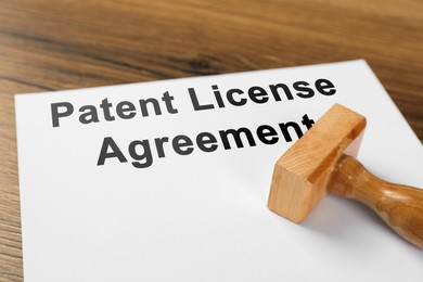 Image of Paper with Patent License Agreement text and stamp tool on wooden table, closeup