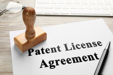 Image of Paper with Patent License Agreement text, pen and stamp tool on wooden table, closeup