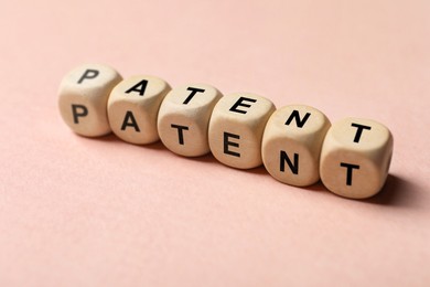 Image of License. Word Patent made of wooden cubes with letters on pink background, closeup