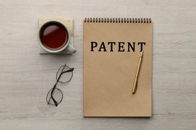 Image of License. Word Patent in notebook, eyeglasses, pen and tea on wooden table, flat lay