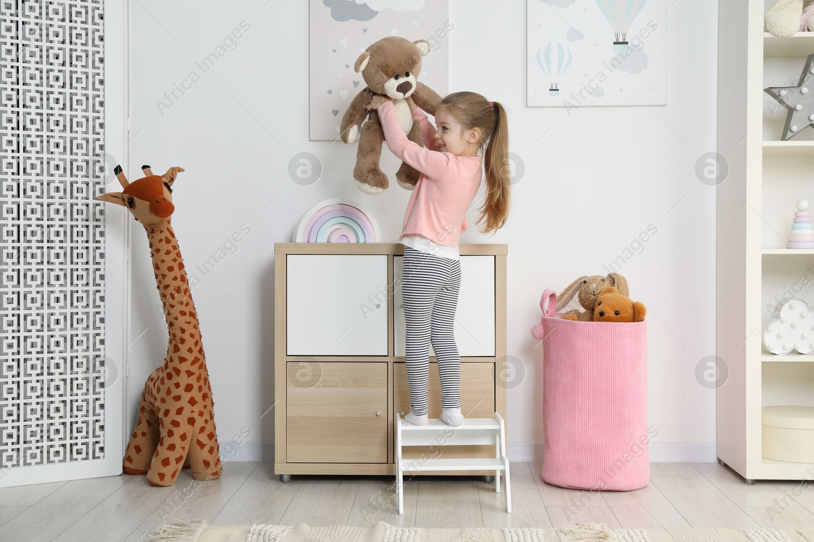 Photo of Little girl standing on step stool and playing with toys indoors