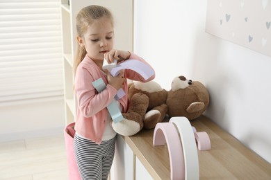 Photo of Little girl playing with toys on chest of drawers indoors