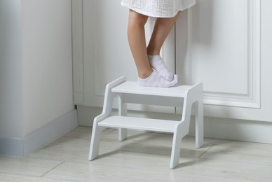 Photo of Little girl standing on step stool indoors, closeup