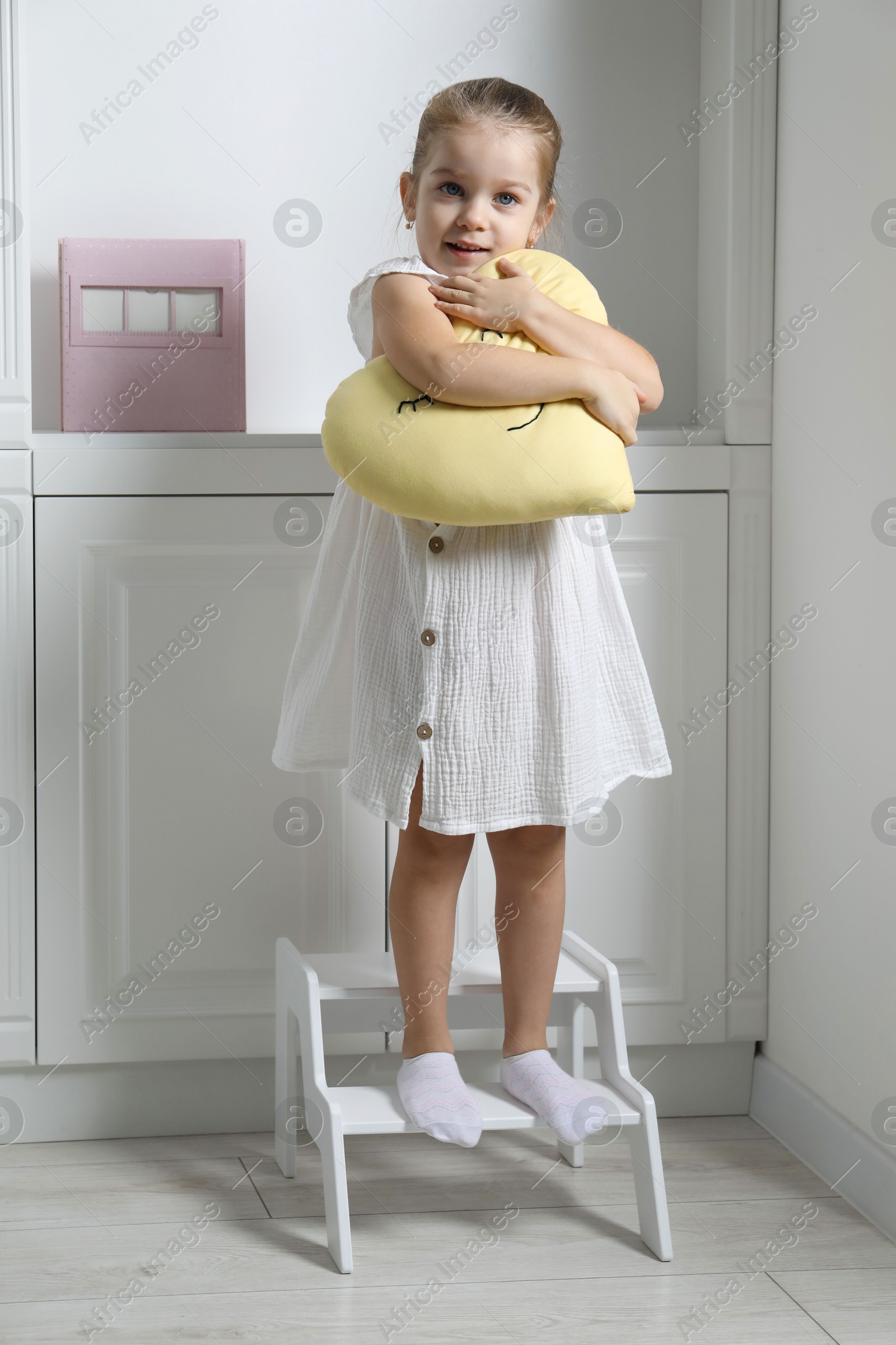 Photo of Little girl with toy standing on step stool indoors