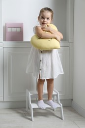 Little girl with toy standing on step stool indoors