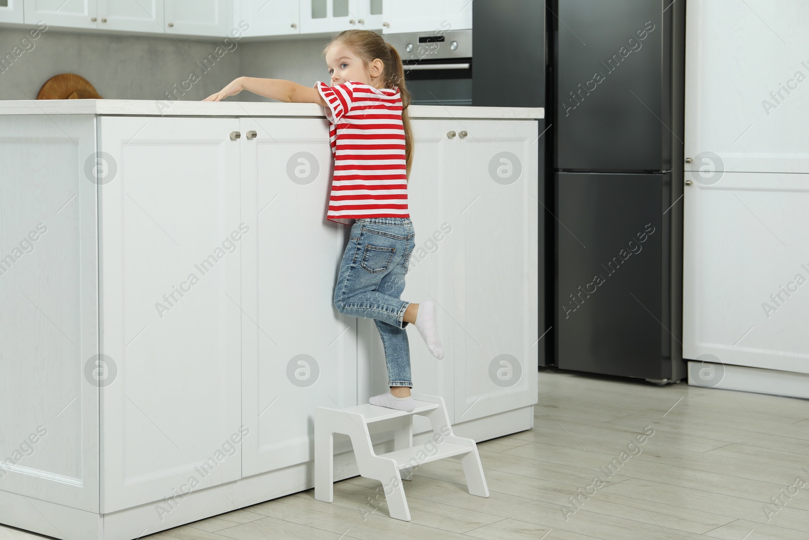 Photo of Little girl standing on step stool and reaching towards counter in kitchen