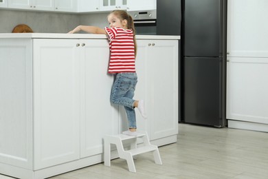 Photo of Little girl standing on step stool and reaching towards counter in kitchen