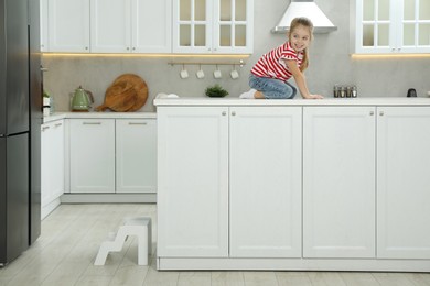 Photo of Little girl sitting on counter near step stool in kitchen