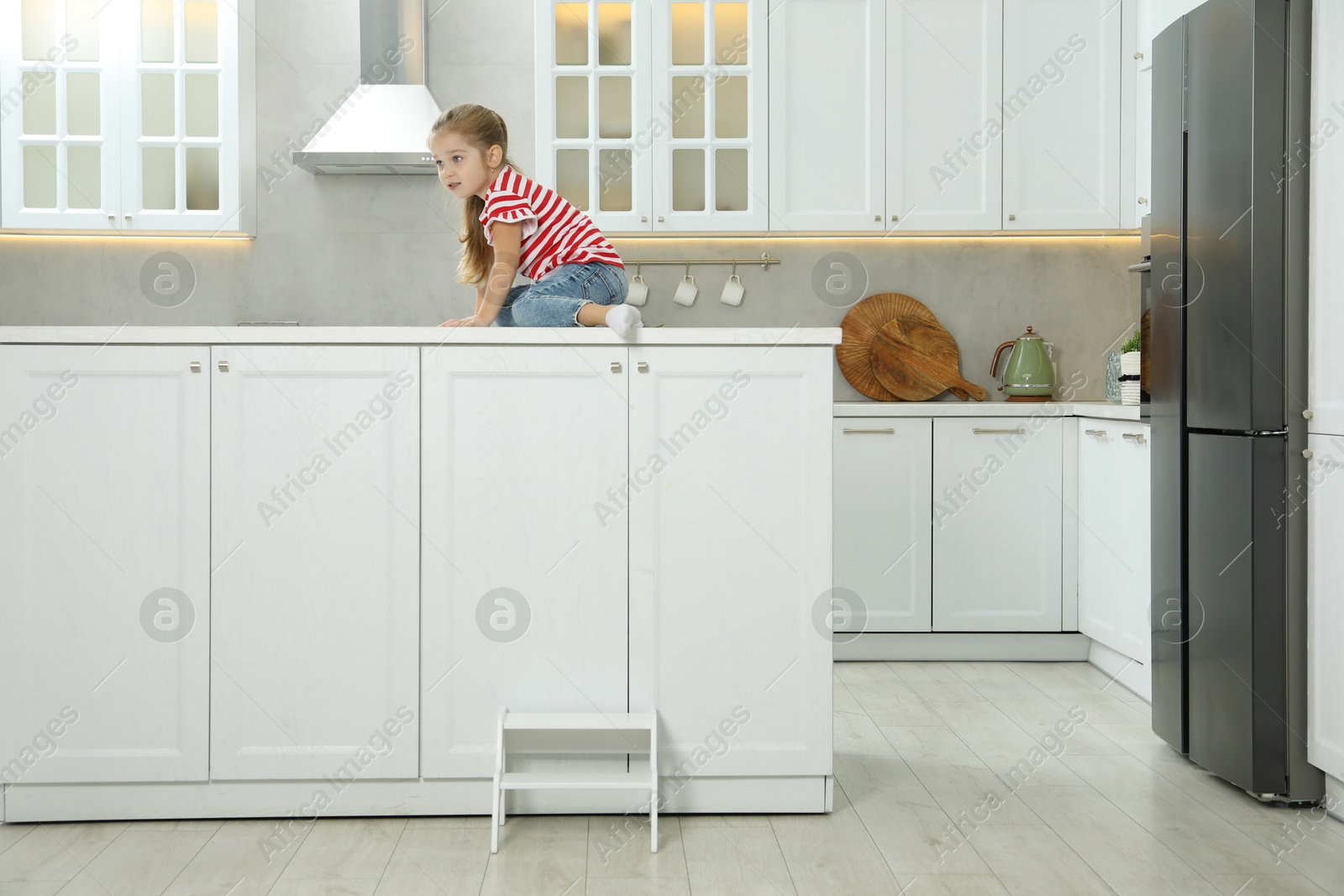 Photo of Little girl sitting on counter near step stool in kitchen