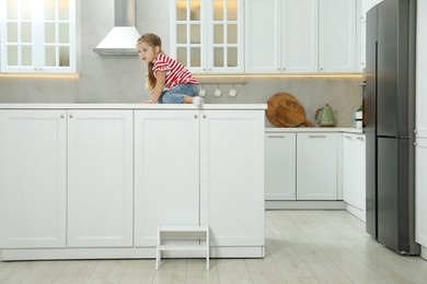 Photo of Little girl sitting on counter near step stool in kitchen