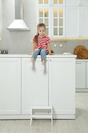 Photo of Little girl sitting on counter near step stool in kitchen