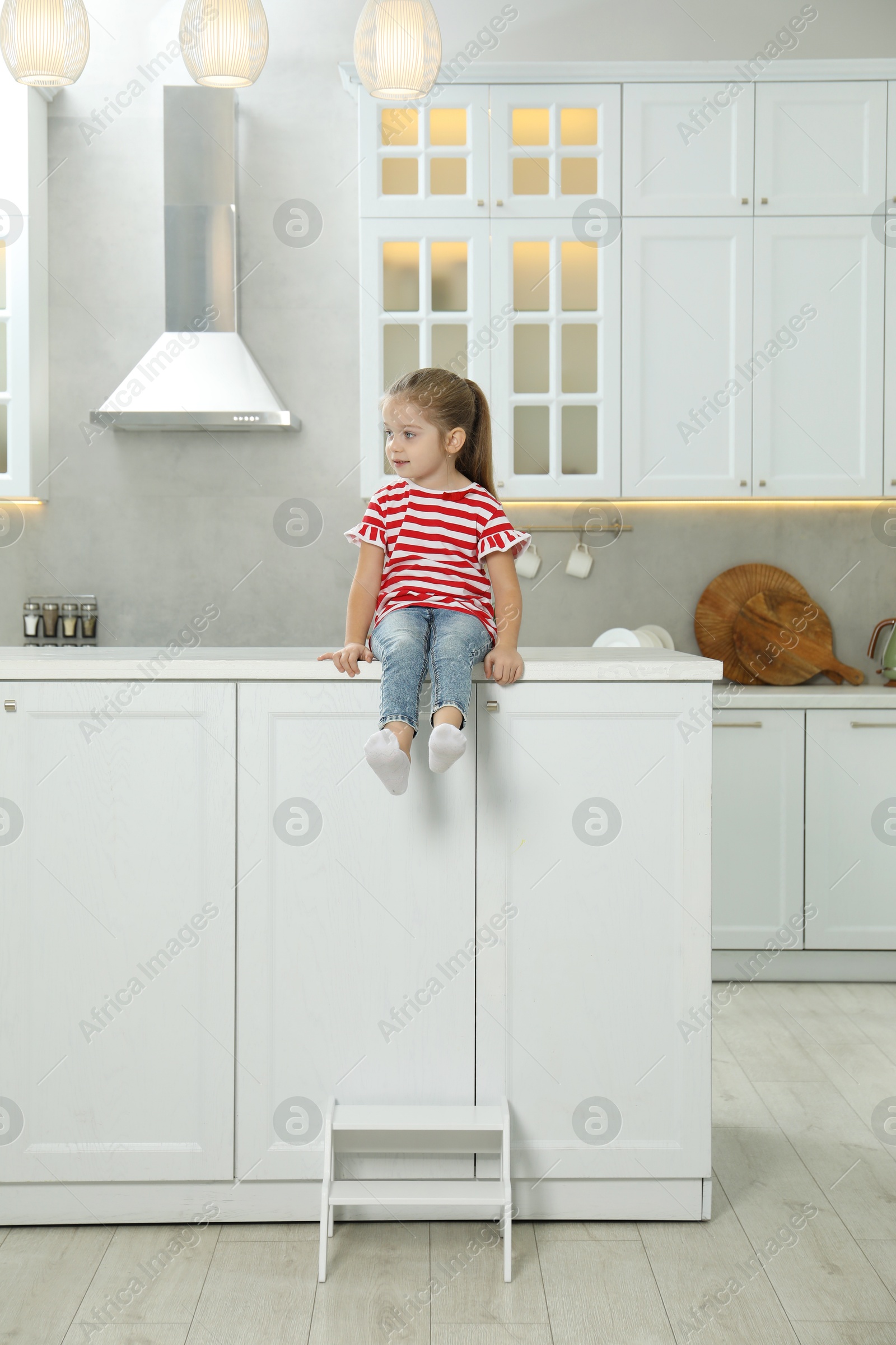 Photo of Little girl sitting on counter near step stool in kitchen