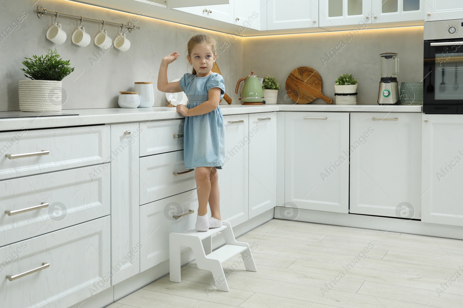 Photo of Little girl standing on step stool and reaching towards counter in kitchen