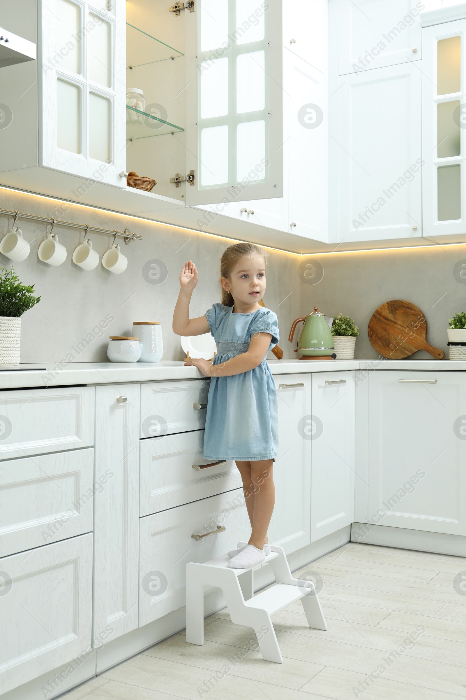 Photo of Little girl standing on step stool and reaching towards counter in kitchen