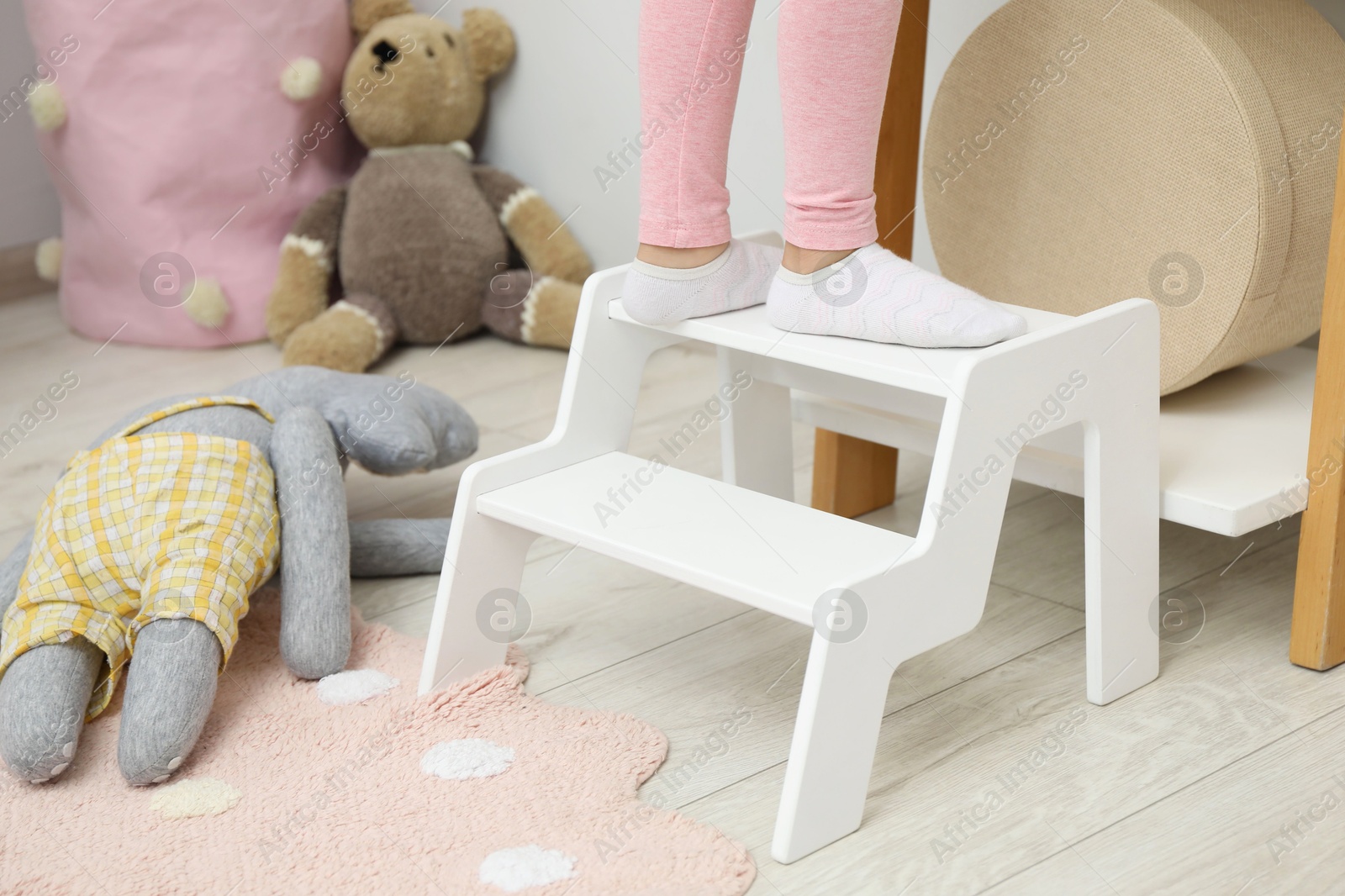 Photo of Little girl standing on step stool indoors, closeup