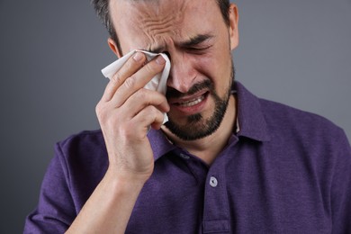 Sad man with paper tissue crying on grey background