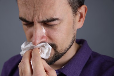 Photo of Sad man with paper tissue crying on grey background, closeup