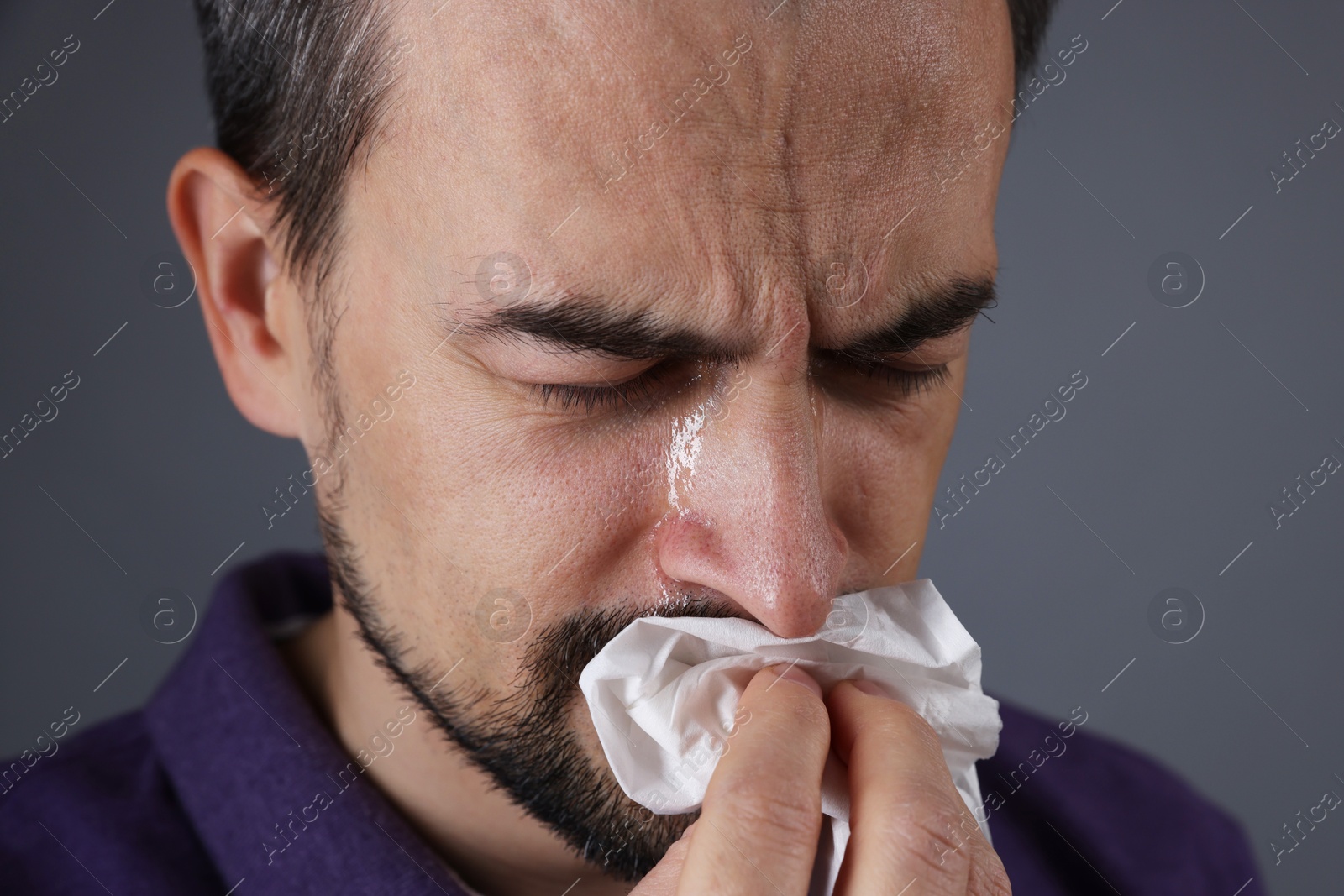 Photo of Sad man with paper tissue crying on grey background, closeup