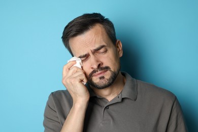 Sad man with paper tissue crying on light blue background