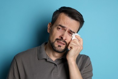 Sad man with paper tissue crying on light blue background