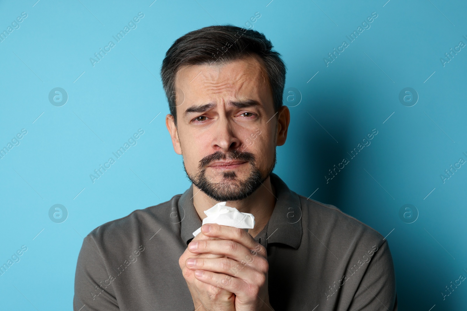 Photo of Sad man with paper tissue crying on light blue background