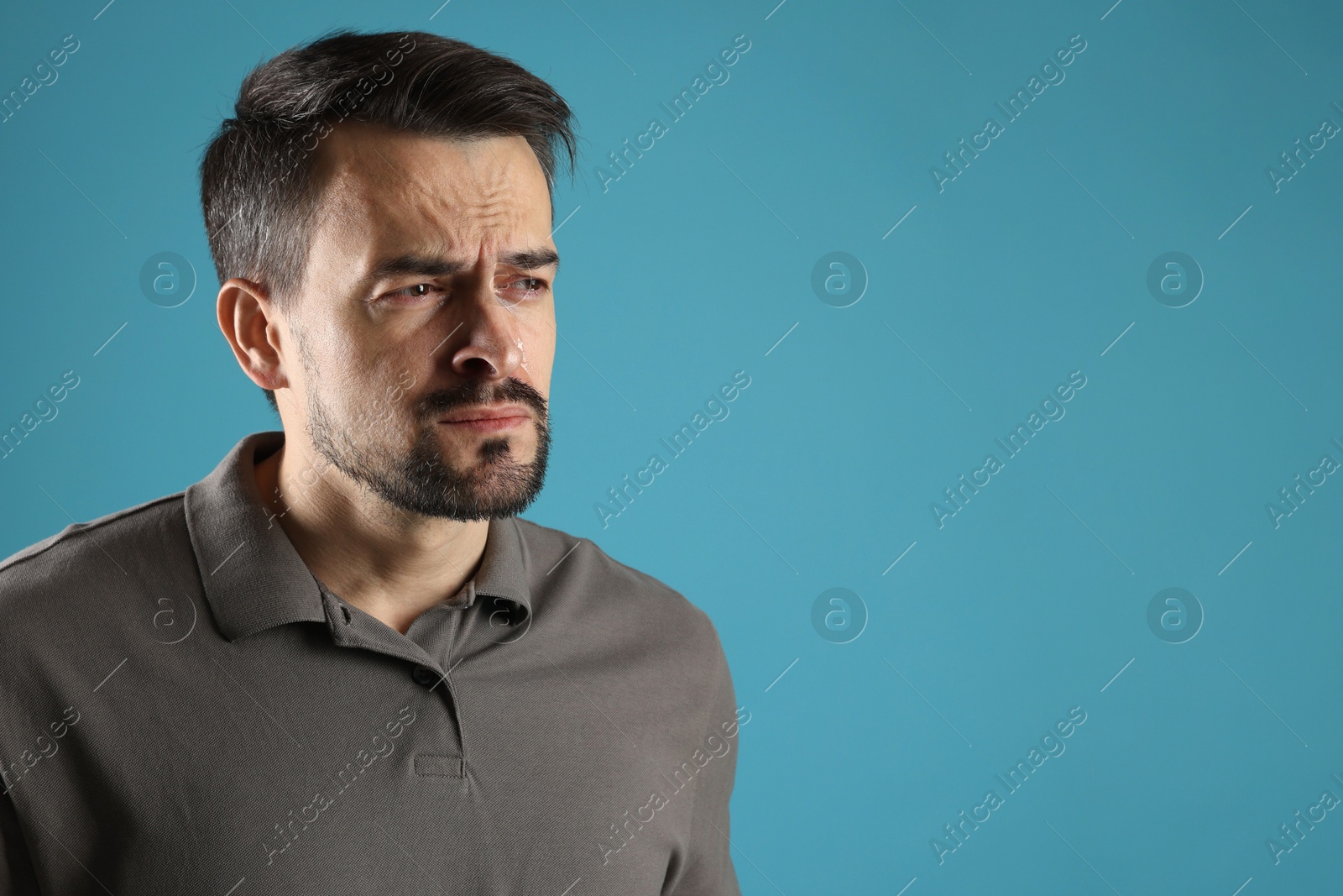 Photo of Sad man crying on light blue background, space for text