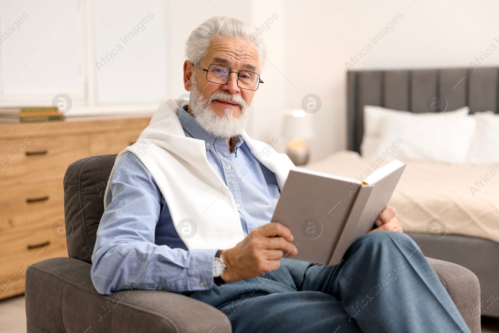 Photo of Handsome bearded man reading book in armchair at home