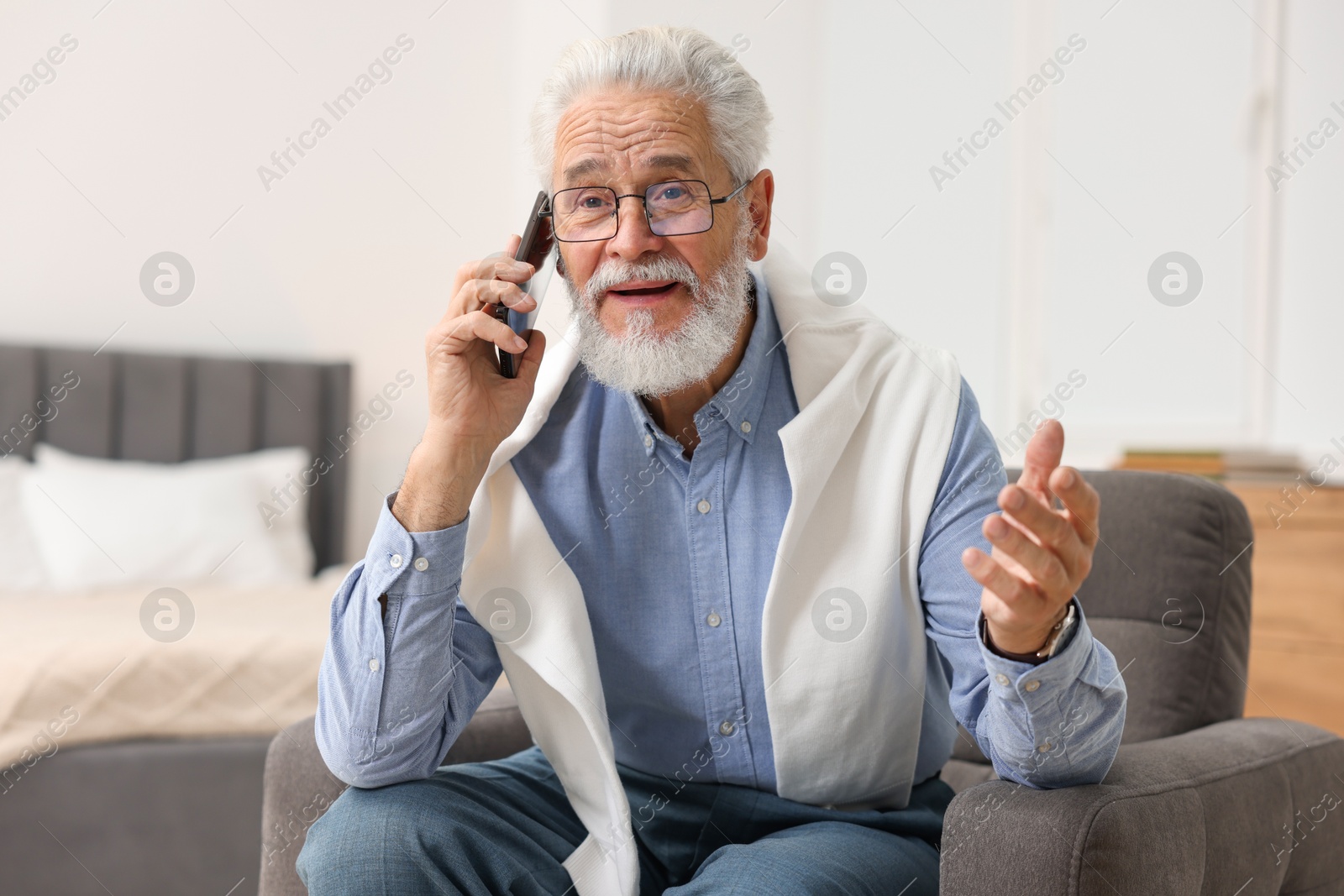 Photo of Handsome bearded man talking on smartphone in armchair indoors