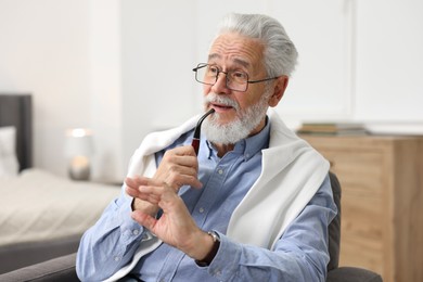 Photo of Handsome bearded man with tobacco pipe in armchair indoors