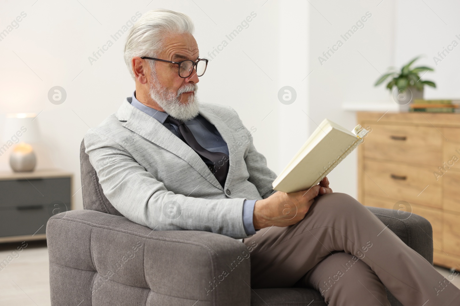 Photo of Handsome bearded man reading book in armchair indoors