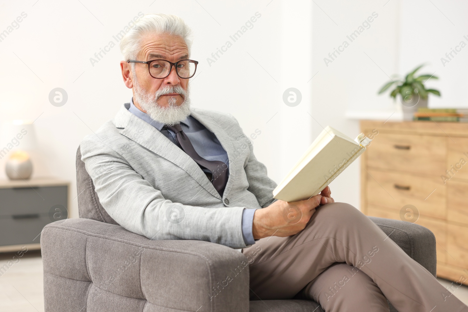 Photo of Handsome bearded man reading book in armchair indoors