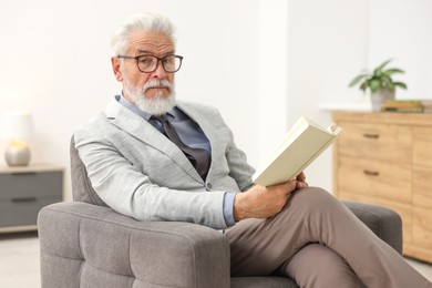 Photo of Handsome bearded man reading book in armchair indoors