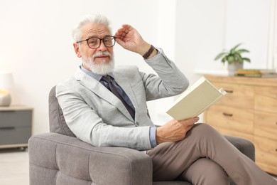 Photo of Handsome bearded man reading book in armchair indoors