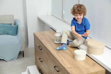 Photo of Little boy with boxes on window sill at home